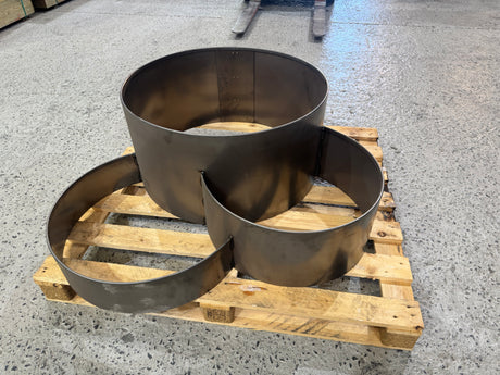 Three various-sized industrial round metal planter or fire pit liners displayed on a wooden pallet in a warehouse.